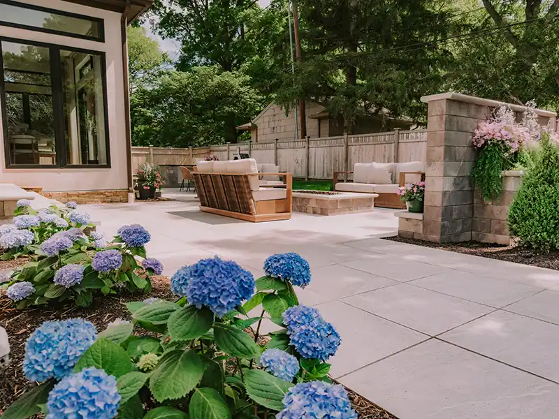 Unilock Fire Pit with GeoCeramica Porcelain Pavers Outdoor seating area surrounding a custom gas fire pit built with Unilock Pisa 2XL Smooth block and limestone coping on a GeoCeramica porcelain patio.
