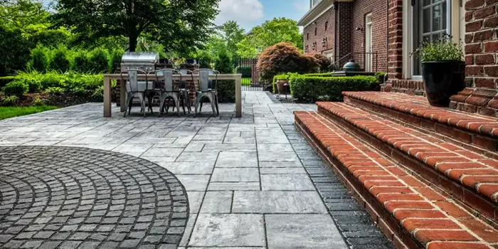 custom paver patio with circular cobblestone inlay New Albany Ohio large format paver patio with outdoor dining area Central Ohio decorative circular paver inlay patio design New Albany Ohio backyard patio with outdoor grill station and pavers Ohio custom patio installation at brick home in New Albany Ohio