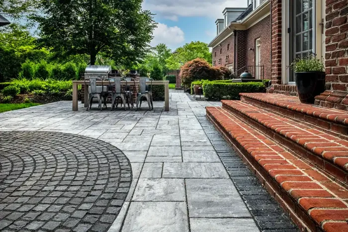 custom paver patio with circular cobblestone inlay New Albany Ohio large format paver patio with outdoor dining area Central Ohio decorative circular paver inlay patio design New Albany Ohio backyard patio with outdoor grill station and pavers Ohio custom patio installation at brick home in New Albany Ohio