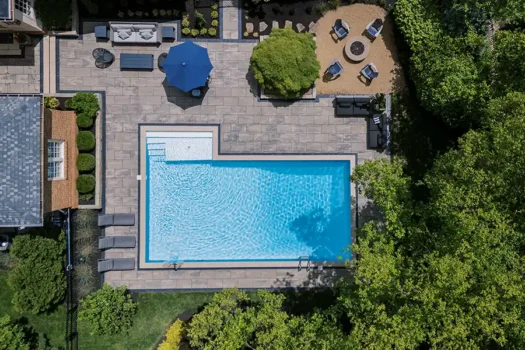 Aerial view of a custom Unilock Beacon Hill XL Smooth paver pool deck with Copthorne Basalt accents, pool coping, outdoor seating and a separate fire pit area in New Albany, Ohio.
