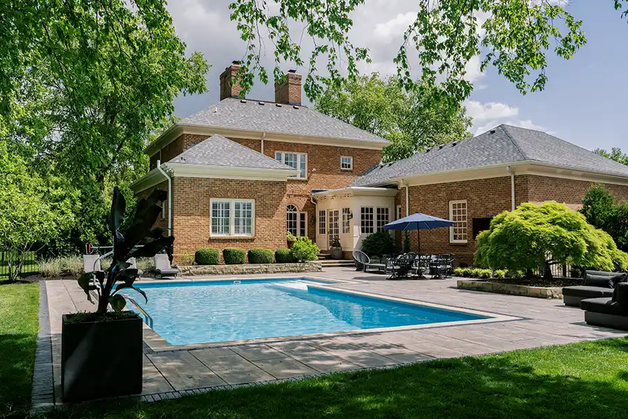 Custom paver pool deck with outdoor dining and lounge areas, natural stone landscape walls and mature plantings at a New Albany, Ohio home.